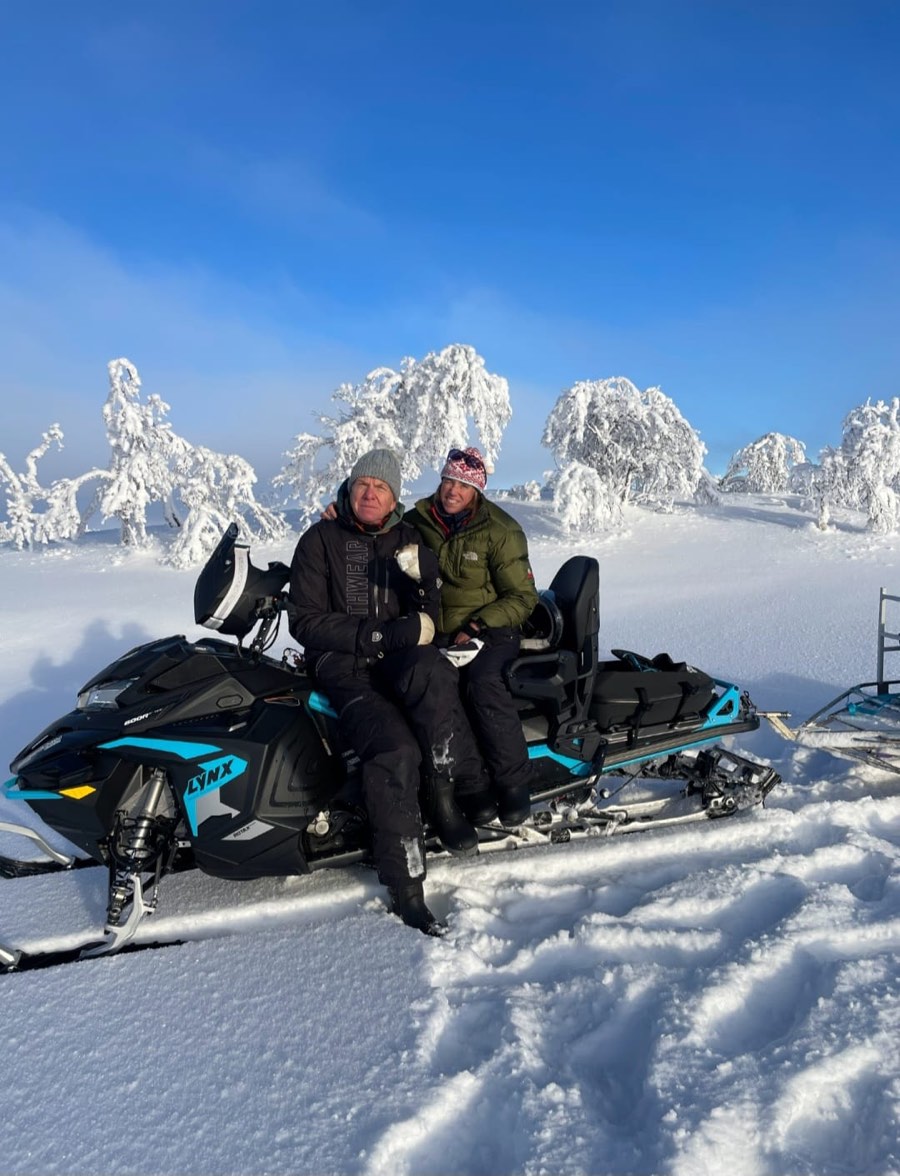 Två personer sitter på en snöskoter i ett snötäckt vinterlandskap.
